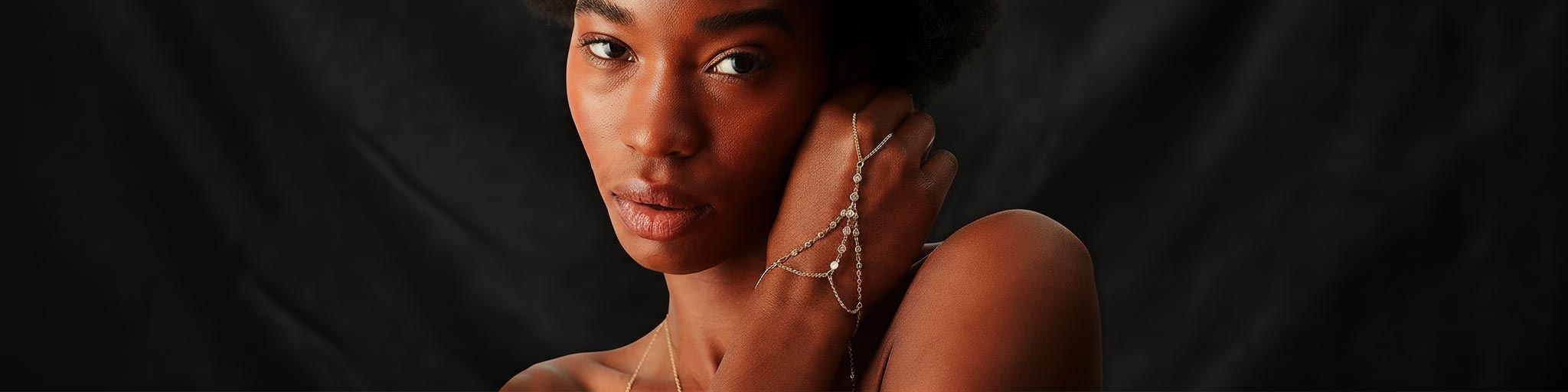 Woman with a gold and diamond hand chain against a dark background