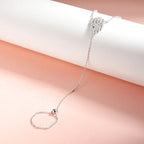 An ornate centerpiece in the middle of a silver white gold hand chain bracelet is connected to a polished silver bead by its fine chains 