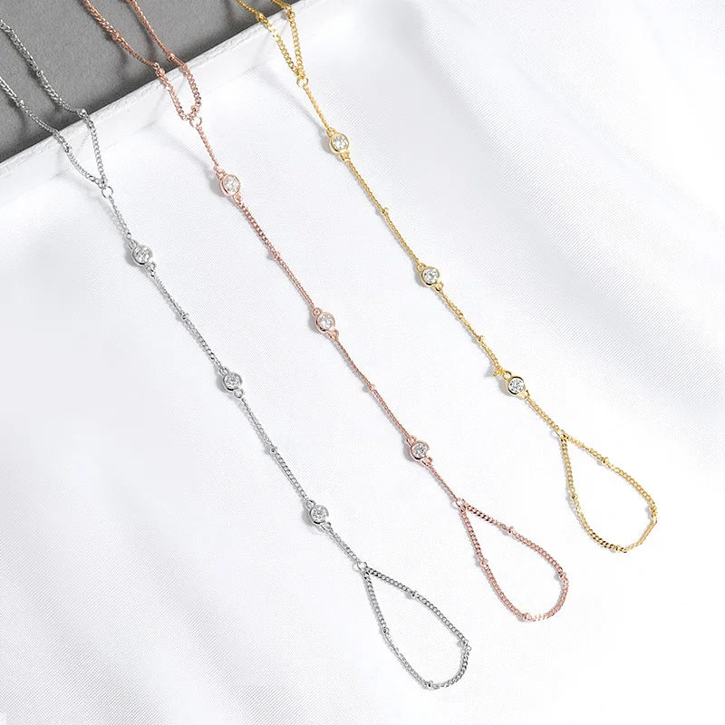 Three hand chain bracelets in gold, silver, and rose gold on a white surface